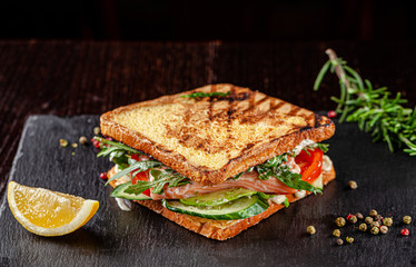 Vegetarian American Cuisine. Homemade toast sandwich with red fish salmon, arugula, cucumbers and tomatoes, white sauce. Sandwich on a black background. copy space text - obrazy, fototapety, plakaty