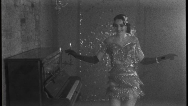 Young happy beautiful woman in bright sparkling luxury silver dress, smiles gown fluttering dances in room near piano, black and white old fashioned film with added noise. 20s stylized carnival party