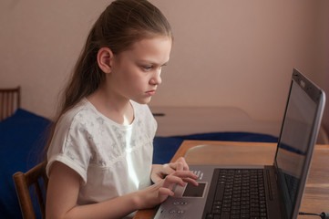 School girl studying at home at a table on a laptop