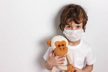 Portrait of kid wearing medical mask with toy monkey on white background. Concept of coronavirus...