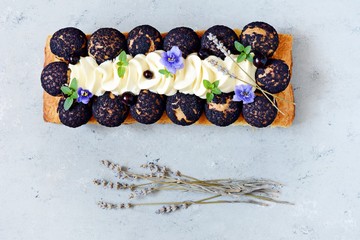 Dessert Saint Onore. Berry pie. Puff pastry tart with profiteroles, butter cream, black currant jam with fresh mint, lavender flowers and berries. Gourmet french dessert on gray background.