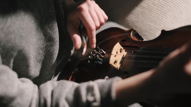 Closeup shot of woman fingers tuning violin strings with the fine tuners after changing strings, moody low light scene at home, hand detail shot