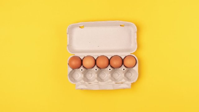Eggs in the cardboard tray move horizontally, then disappear and appear in the box on a yellow background. Top view, stop motion animation