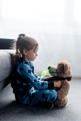 side view of cute child holding teddy bear in respiratory mask