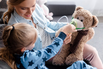 selective focus of kid touching respiratory mask on teddy bear near happy mother