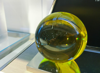 Green glass ball in the form of a sphere with emerald tint on a glass shelf with cold illumination