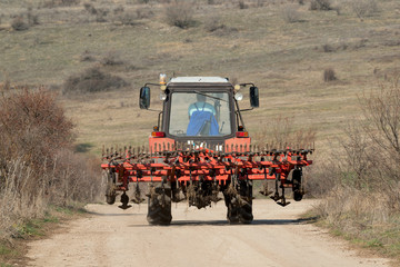 Tractor with plow on rural road against a mountain background.