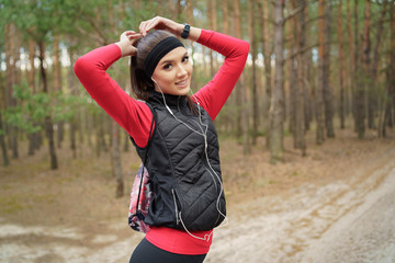 Cute girl is walking in a beautiful forest at the weekend. She is listening  favorite music. She has a beautiful smile. Healthy lifestyle and relax concept.