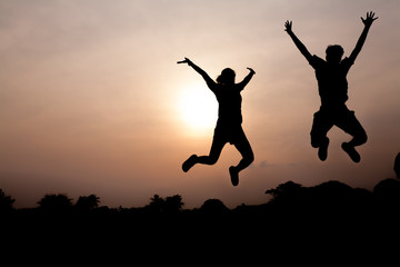 Silhouette of two young adults jumping cheerfully in orange sky background, freedom concept