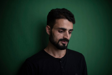 Fototapeta premium Portrait of young brunette Indian Kashmiri man in casual tee shirt in green copy space studio background. lifestyle and fashion.