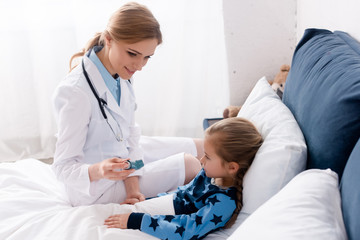 Fototapeta na wymiar happy doctor in white coat holding inhaler near asthmatic child