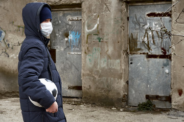concept of epidemic and quarantine - a boy with a face mask and a ball alone on the street in the city