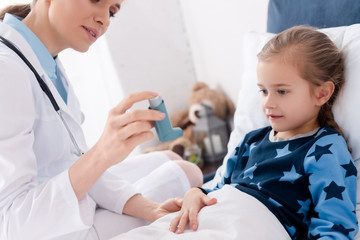Fototapeta premium doctor in white coat holding inhaler near asthmatic child