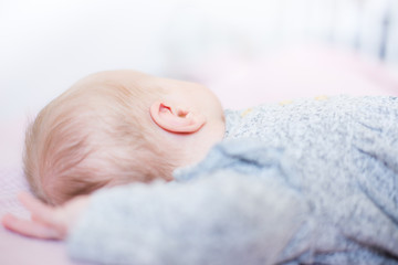Baby ear close up, baby girl lying down on a light pink blanket