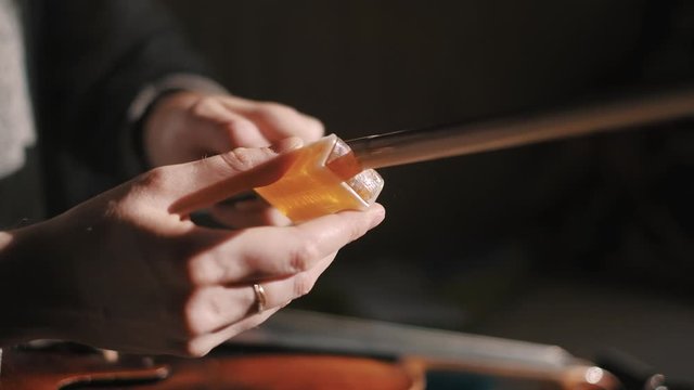 Young woman fiddler applying rosin to the violin bow hair to create friction between the bow and the strings, closeup shot, dust specks particles floating in air