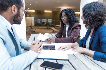 Business partners consulting legal expert in outdoor cafe. Business man and women sitting at table outside, checking and discussing documents. Expertise concept