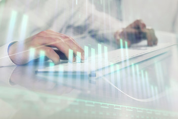 Double exposure of graph with man typing on computer in office on background. Concept of hard work. Closeup.