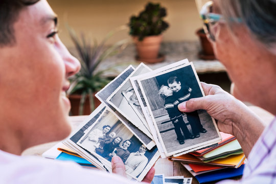 Coronavirus emergency. Senior grandmother stays home with nephew  looking old photo of 1950 and 1959. Two real people avoiding infection by COVID-19 coronavirus