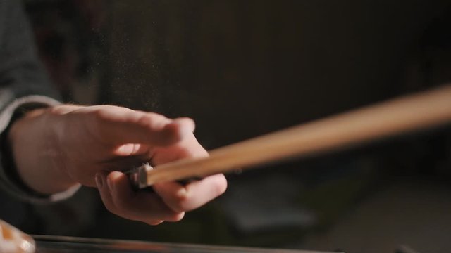Young woman fiddler removing excess of rosin from the fiddlestick violin bow, closeup shot, dust specks particles floating in air