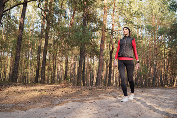 Caucasian woman  is walking in a suburban forest after work. She is listening  favorite music. She has a beautiful smile. Healthy lifestyle and relax concept.