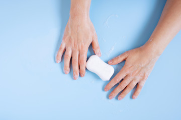 Fototapeta premium Female hands holding the piece of white soap and foam on the blue background