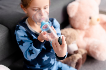 selective focus of sick kid using inhaler with spacer near soft toys - obrazy, fototapety, plakaty