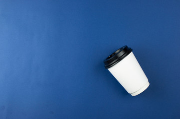 single hot coffee in white paper cup with black lid on blue background