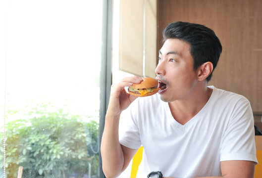 A man enjoy eating with her burger in hands,Asian man open his mouth for biting burger,Men eat burgers without knowing the danger of Junk Food.,Selective focus