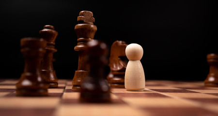 Wooden figures (businessman) standing confront of chess king and being in the chess circle. New business players are facing challenges. The management or leadership, analysis, strategy concept.