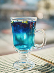 Amazing blue violet color butterfly pea flower blue tea in latte macchiato glass on window sill liten noon hard sunlight
