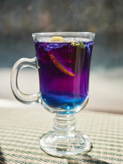 Amazing blue violet color butterfly pea flower blue tea in latte macchiato glass on window sill liten noon hard sunlight