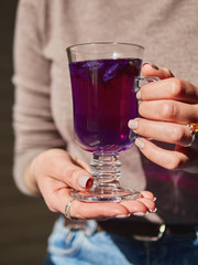 Woman's hands holding amazing blue violet color butterfly pea flower blue tea in latte macchiato glass near window liten noon hard sunlight