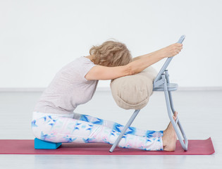 Senior woman doing yoga with chair in a gym. Stretching exercises