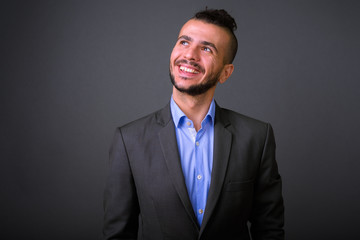 Portrait of happy bearded Turkish businessman in suit thinking