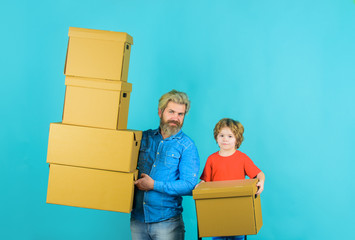 Moving, home and family concept. Father and son holds cardboard boxes. Father holds stack cardboard boxes and son helping him. Prepare for moving. Father and son with shipping boxes. Packaging things.