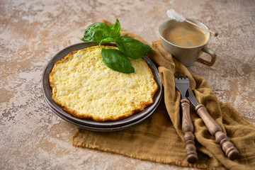 Frittata or omlette with fresh basil and a cup of coffee on light yellow table. Italian Breakfast, horizontal format