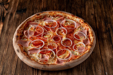 Close up of classic italian pizza with ham, onion rings and tomato,
