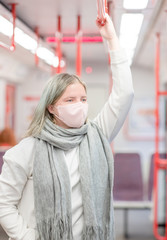 Young woman wearing protective mask against virus and air pollution in public transport holding on to the handrail