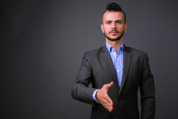Portrait of handsome bearded Turkish businessman in suit giving handshake