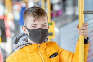 Boy wearing protective mask holding on to the handrail in the bus
