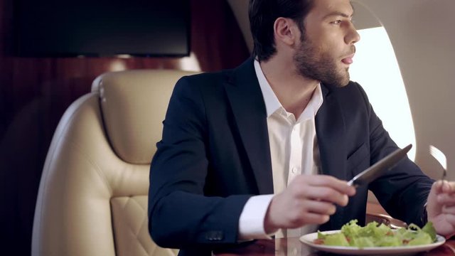 handsome businessman eating fresh salad while traveling by plane