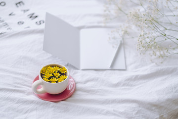 Сup with yellow flowers inside, on a white bed in the morning with notepad and pen. Spring background