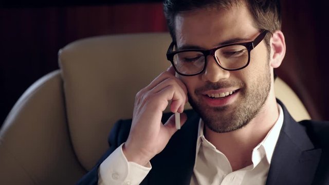 smiling businessman reading newspaper and talking on smartphone in plane