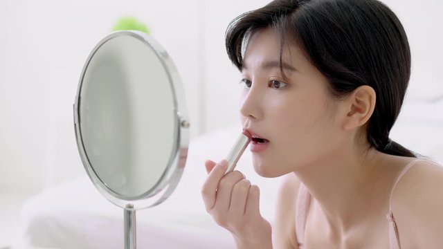 Beautiful young asian woman applying lipstick pink with style bright and shiny on mouth, beauty girl looking mirror for makeup cosmetic with lip elegance, fashion make up with luxury and sexy.
