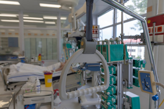 Hospital Bed Trapeze, On Background Patient  Connected To Medical Ventilator In ICU In Hospital, A Place Where Can Be Treated Patients With Pneumonia Caused By Coronavirus Covid 19.