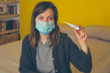 handsome girl brunette with Coronavirus wears protective mask and reads his temperature on a electronic thermometer. man at home with flu covid19 virus