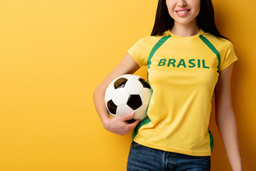 Fototapeta cropped view of smiling female football fan holding ball on yellow obraz