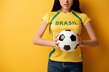 cropped view of angry female football fan holding ball on yellow