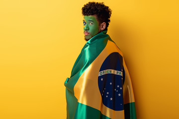 african american football fan with painted face wrapped in brazilian flag on yellow