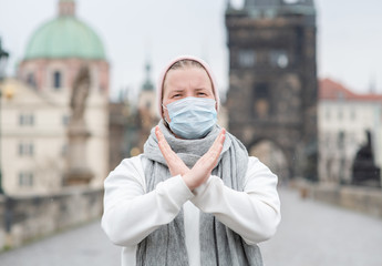 Woman wearing medical mask shows stop gesture on Charles Bridge in Prague. Coronavirus epidemic...